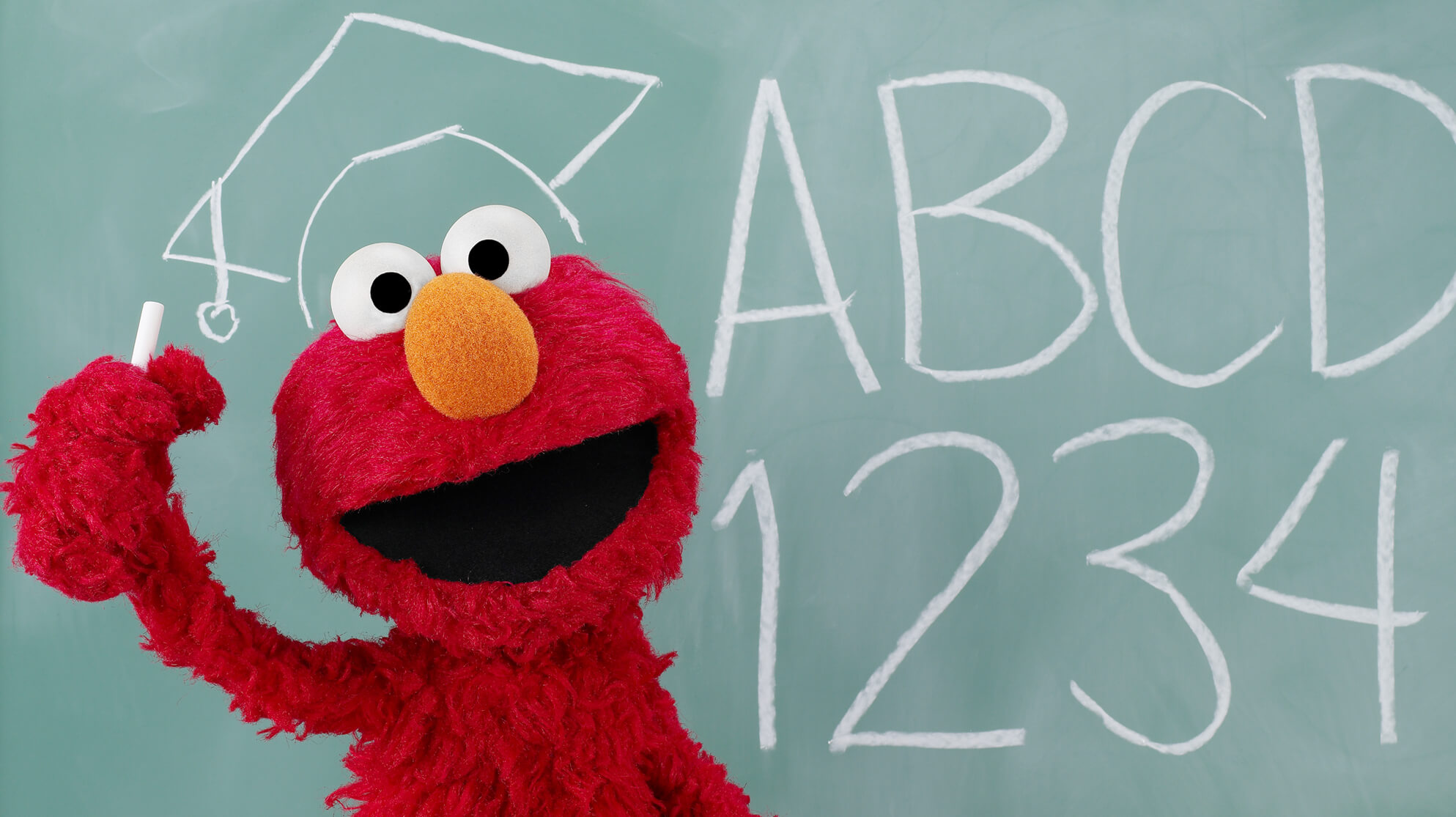 Elmo in front of a chalkboard